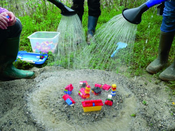 Legosteine werden von Menschen in Gummistiefeln mit Gießkannen begossen
