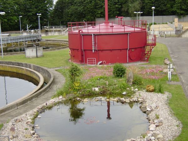 Blick auf eine kleinere Kläranlage mit Teich, Becken und Gasturm
