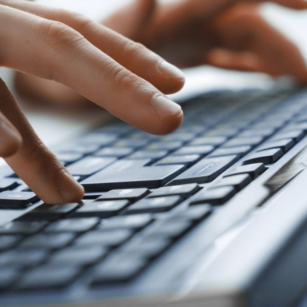 Eine Person bedient zweihändig eine Computertastatur, wobei die linke Hand und der größte Teil der Tastatur undeutlich zu sehen ist und die rechte Hand im Vordergrund deutlich.