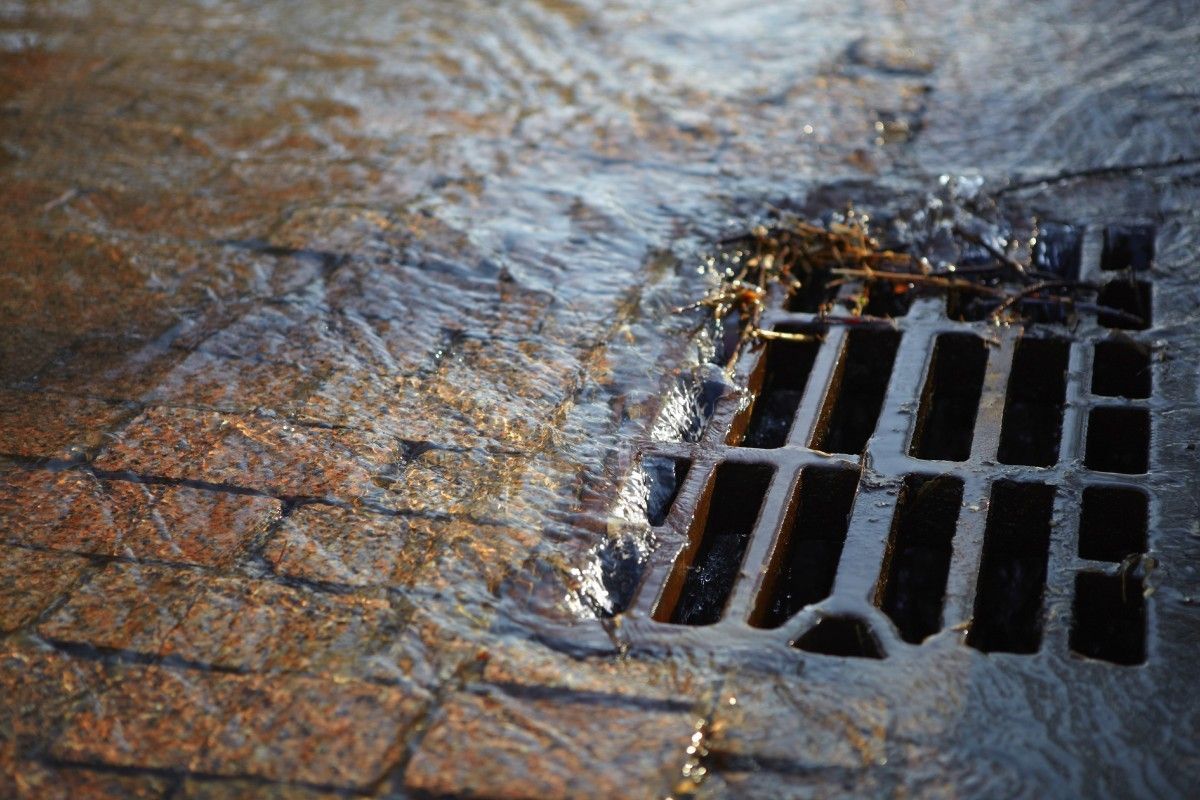 Abwasser läuft in einen vergitterterten Einlaufschacht für Strassenabwässer am Rand einer gepflasterten Straße.