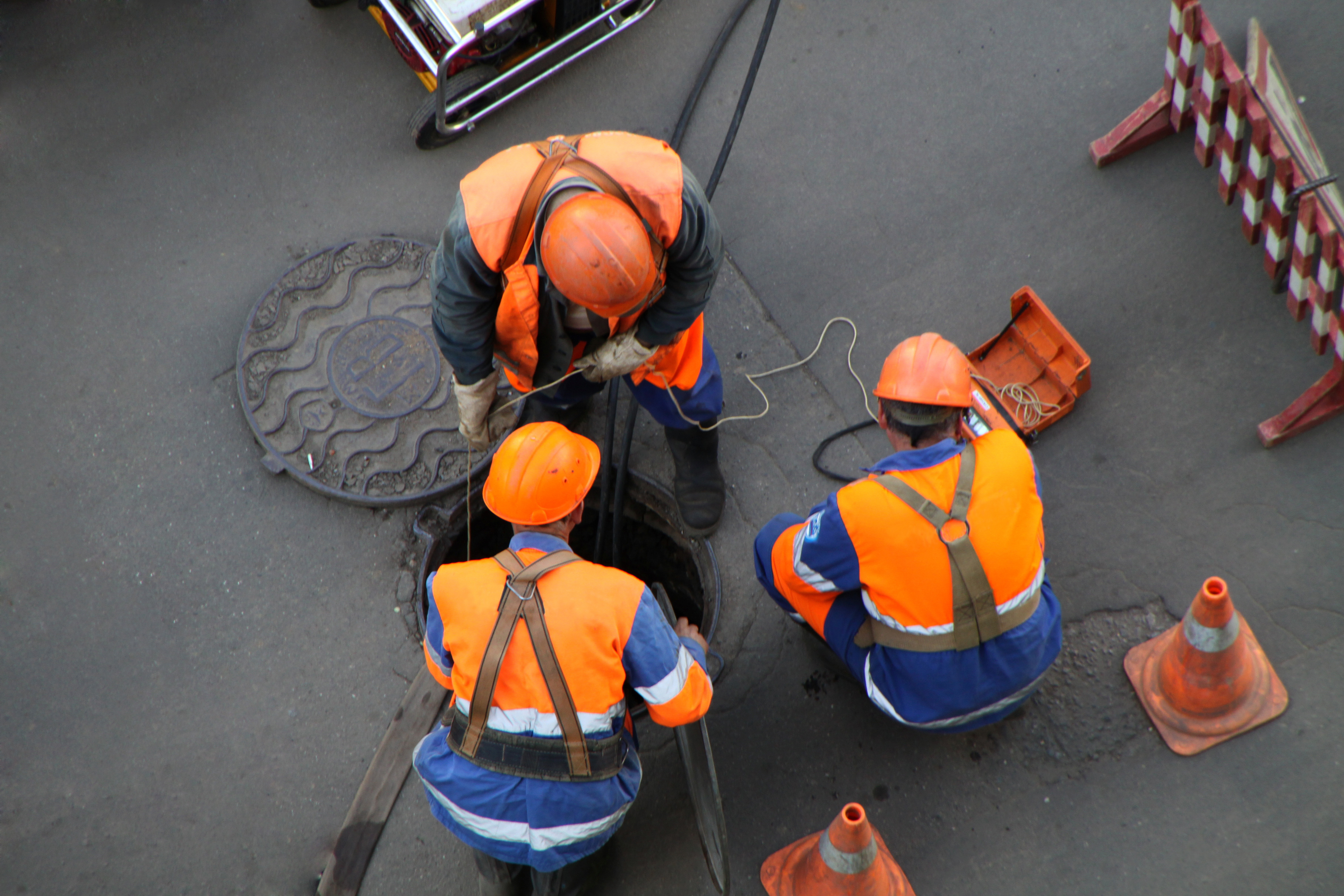 Drei Arbeiter mit Schutzhelmen an geöffnetem Kanaldeckel